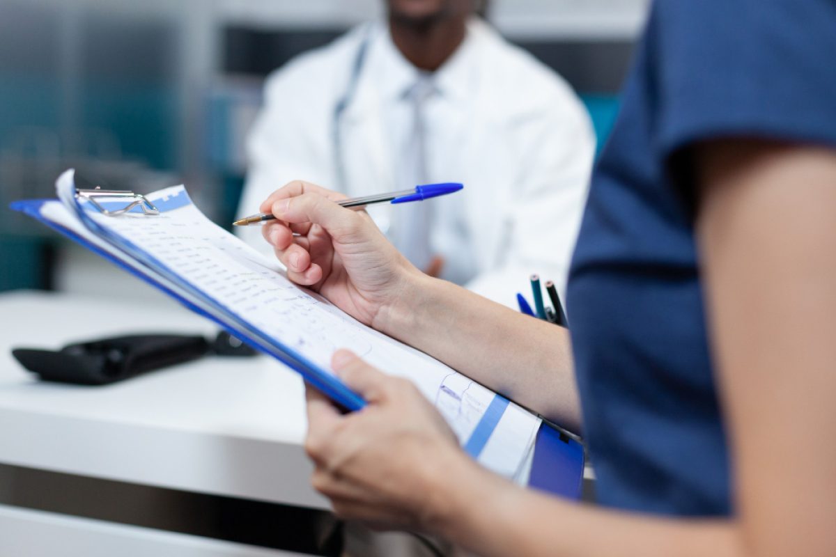 Patient filling out a patient experience survey on a clipboard during a medical consultation.